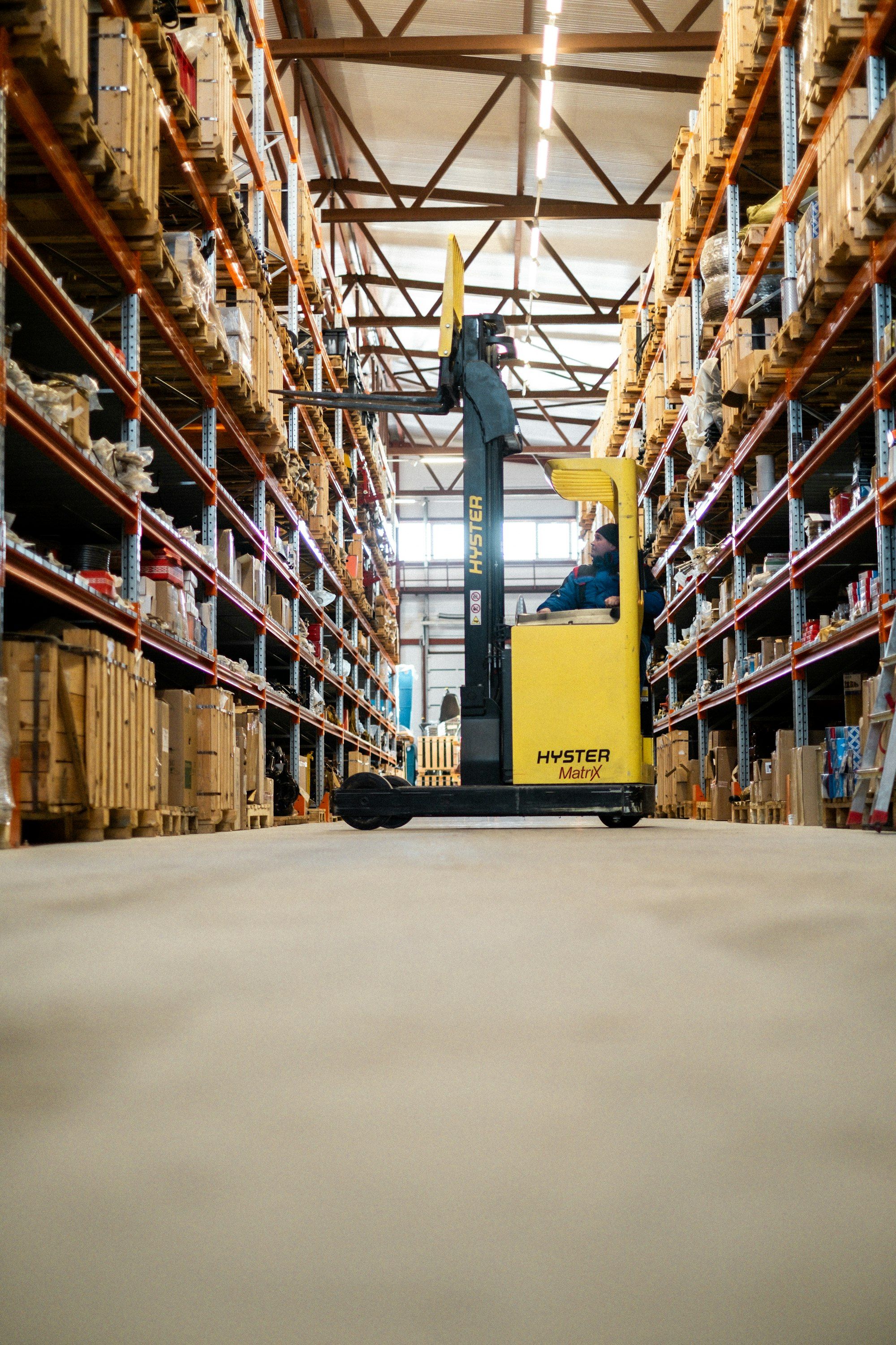 Warehouse worker on a ladder reaching for stock on high shelving